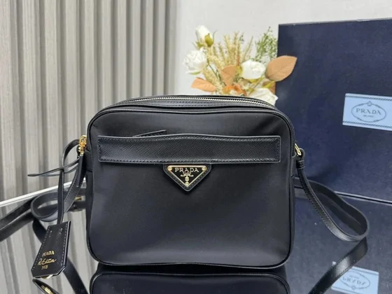 A black crossbody bag with a triangular metal plaque, photographed on a table